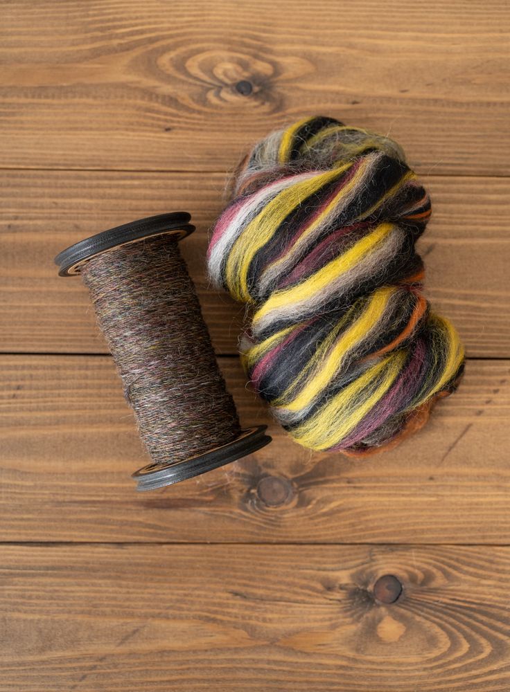 Yarn on the bobbin and the tops alongside on a wood background, revealing that there’s also some raspberry pink in the top. 