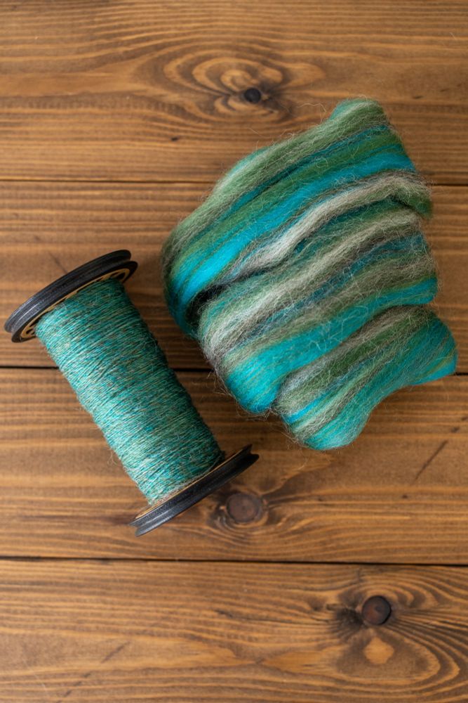 Mineralogy ‘Malachite Magic’, a top containing green, turquoise, grey and white wool, which spins up to a lovely mid-teal. Pictured in tops form and spun singles on a bobbin. 