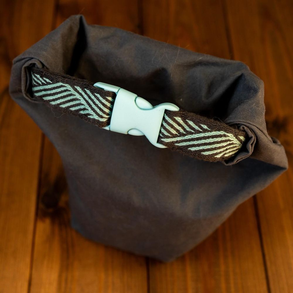 A small, dark grey, roll-top bag, rolled up and fastened with a side-release clasp in a matching aqua colour. 