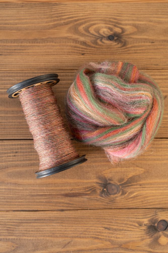 Mineralogy ‘Carnelian’, a top containing green, pink, orange and white wool which spins up to a warm brown/pink. Pictured in tops form and spun singles on a bobbin. 