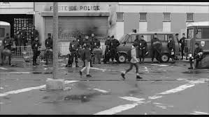 Photo issue du film La Haine montrant la prise complète de l'espace public par des CRS. Des collégiennes se faufilent entre les gardiens de la répression. 
