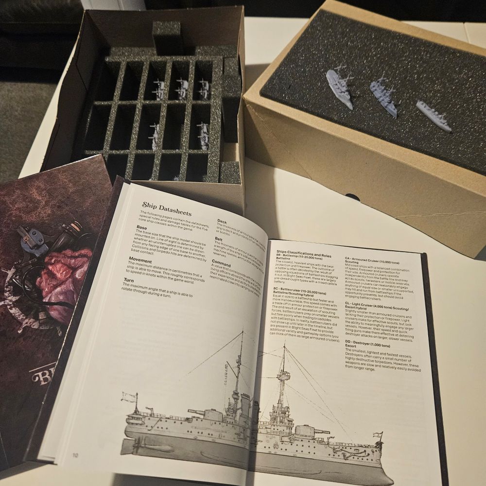 Rulebook spread and box of naval miniatures in foam inserts