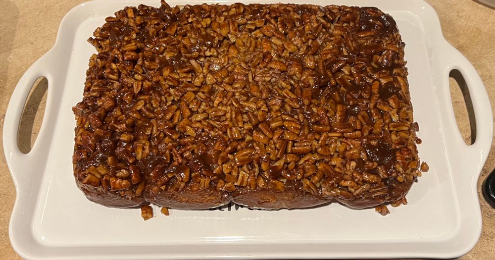 White tray on countertop with maple pecan sticky buns sitting on it. Just an absolute smorgasbord of pecans on top.