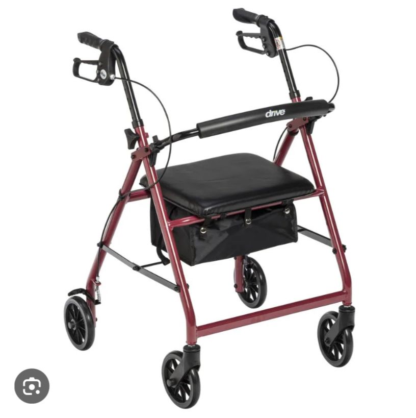 A rollator walker in a product photo, with icon at bottom left showing this was cropped from google image search. This is a red and black walker shown with four plastic wheels down to allow users to sit on a central seat. All wheels descend from four bars that meet in the middle to help with folding. This model has an extra crossbar below the seat in comparison to the other one linked in this post. Not shown is an alternate vertical storage folded position.