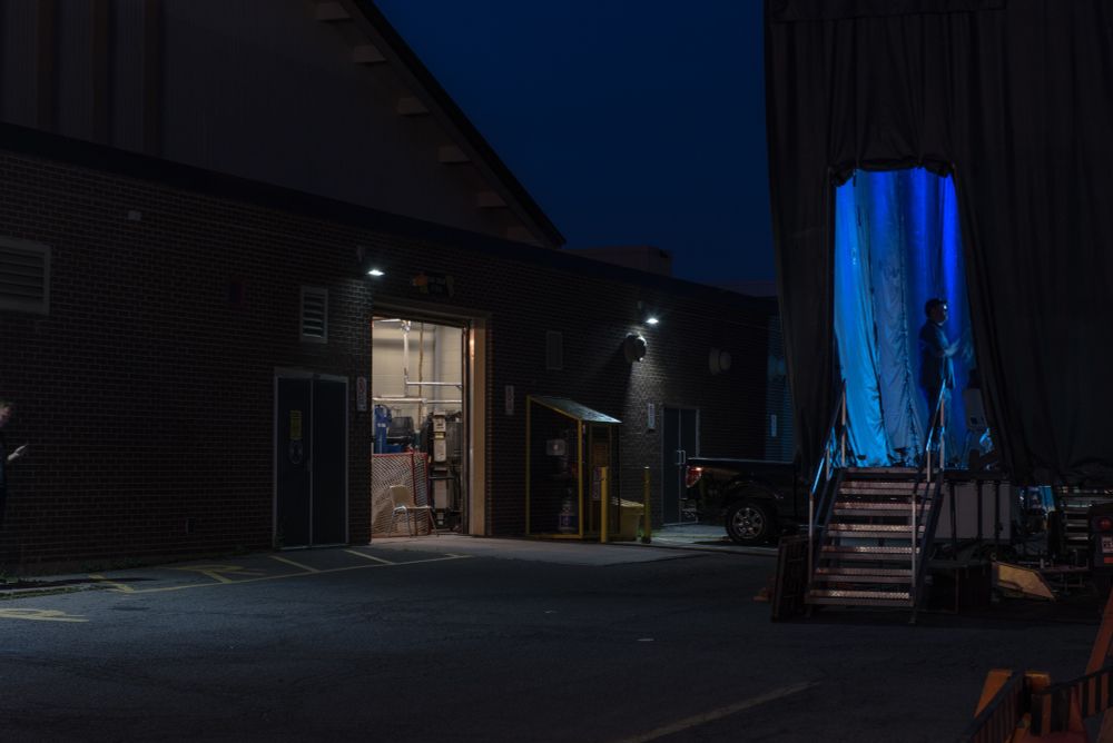 Colour photo of a night scene with light from an open arena door and blue light illuminating a curtain on a mobile performance stage.