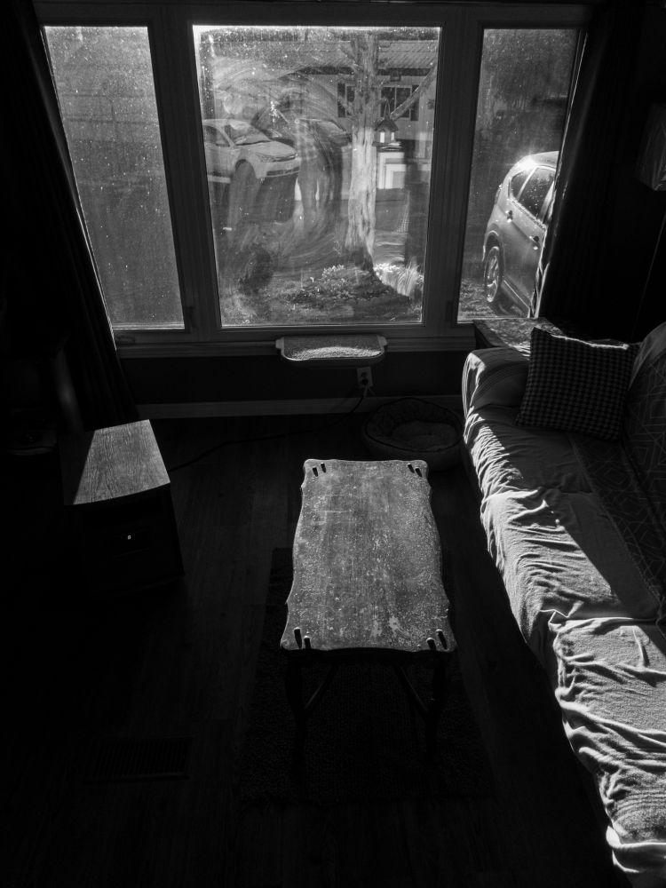 Outside light comes through a window into the trailer, highlighting the surface textures of weathered furniture in a high contrast black and white scene.