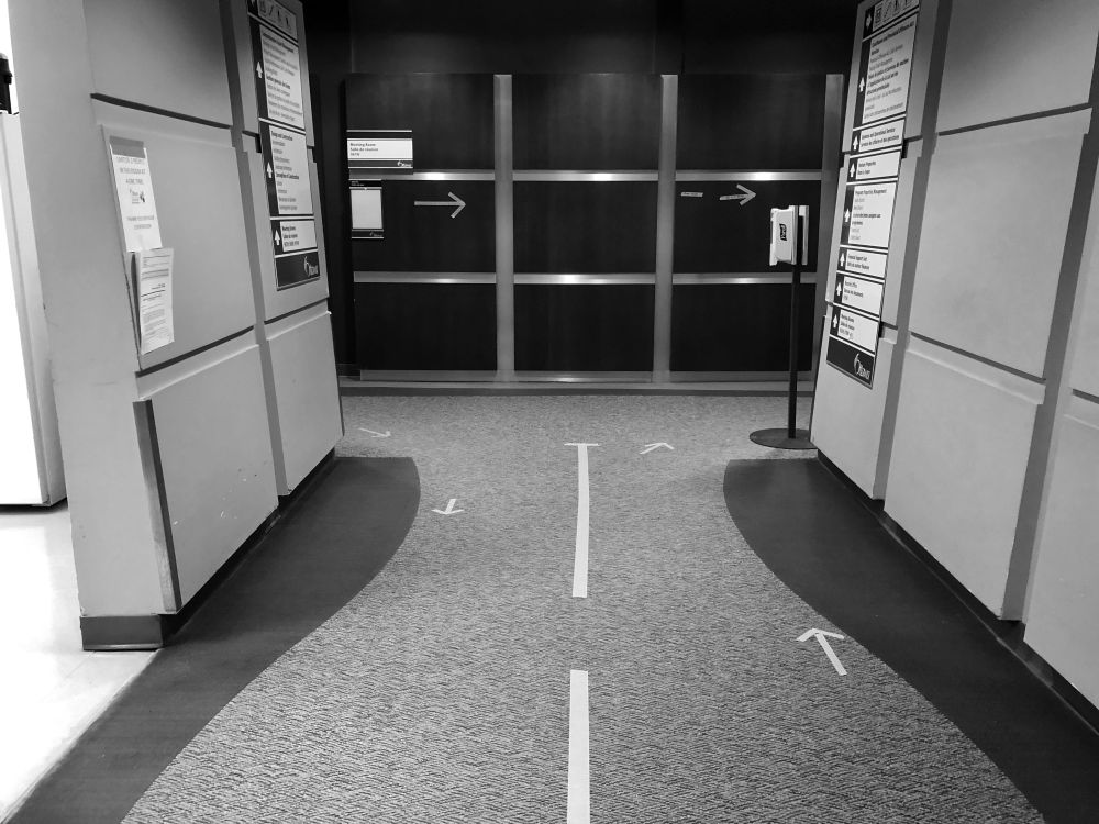 Black and white image of intersecting office hallways with added directional markings during COVID pandemic. Taken May 19, 2020 in Ottawa, Ontario.