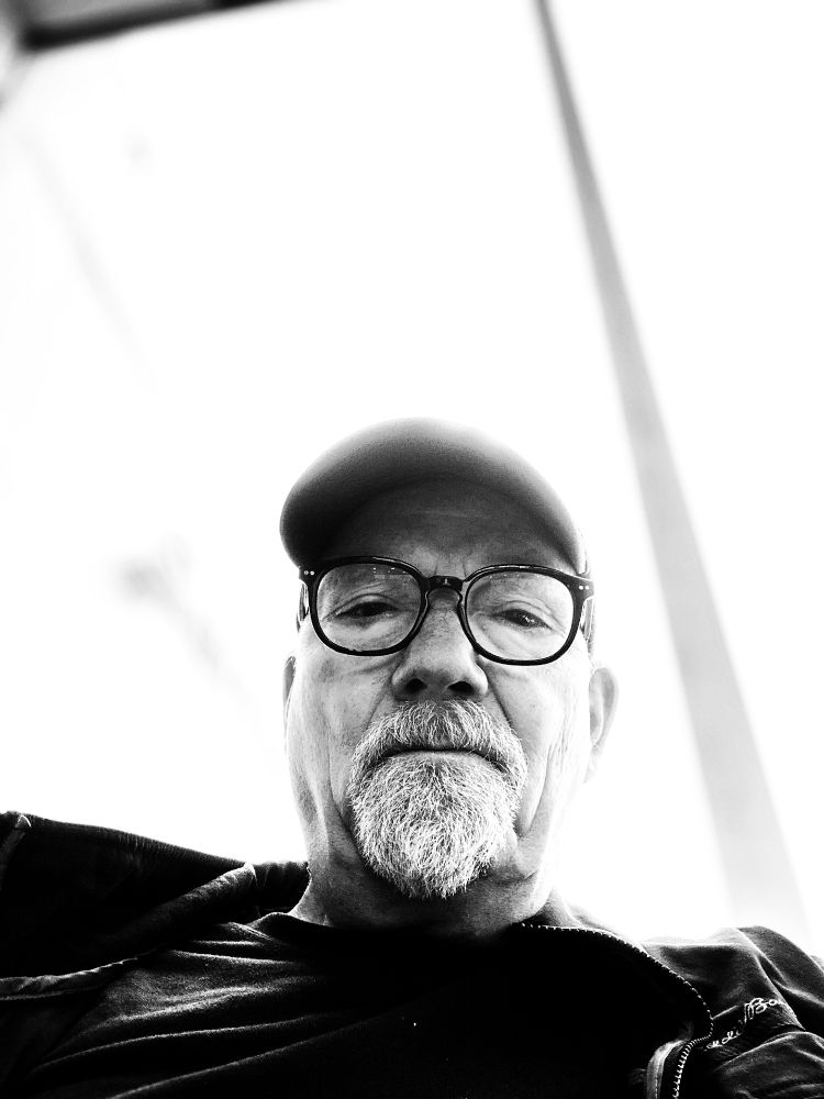 Black and white photograph of this guy looking down at his phone, from the point of view of the phone.