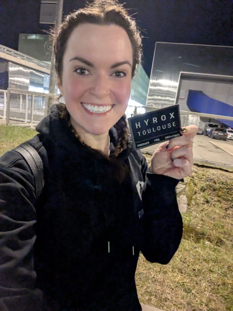 Emma holding a hyrox patch smiling