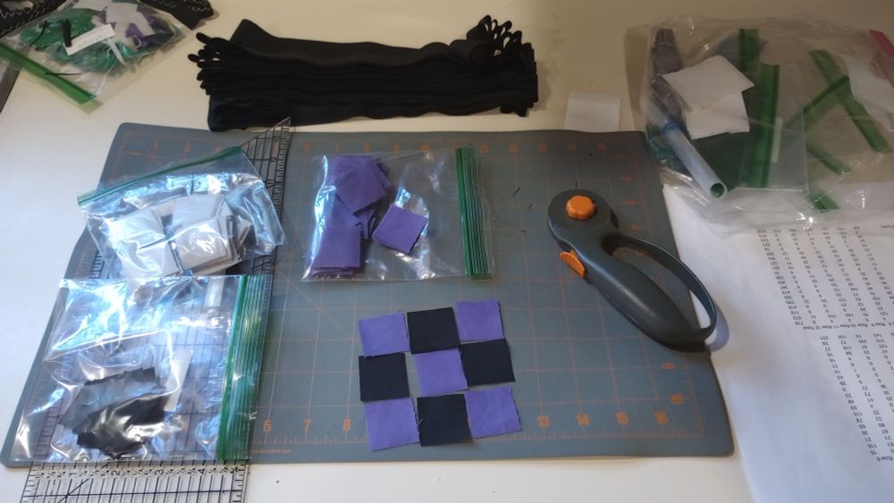 workspace with cut fabric, rotary cutter, mat. ruler and small plastic bags with fabric squares in them.