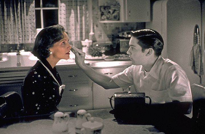 Screenshot from pleasantville, black and white male character is putting makeup on in color female character