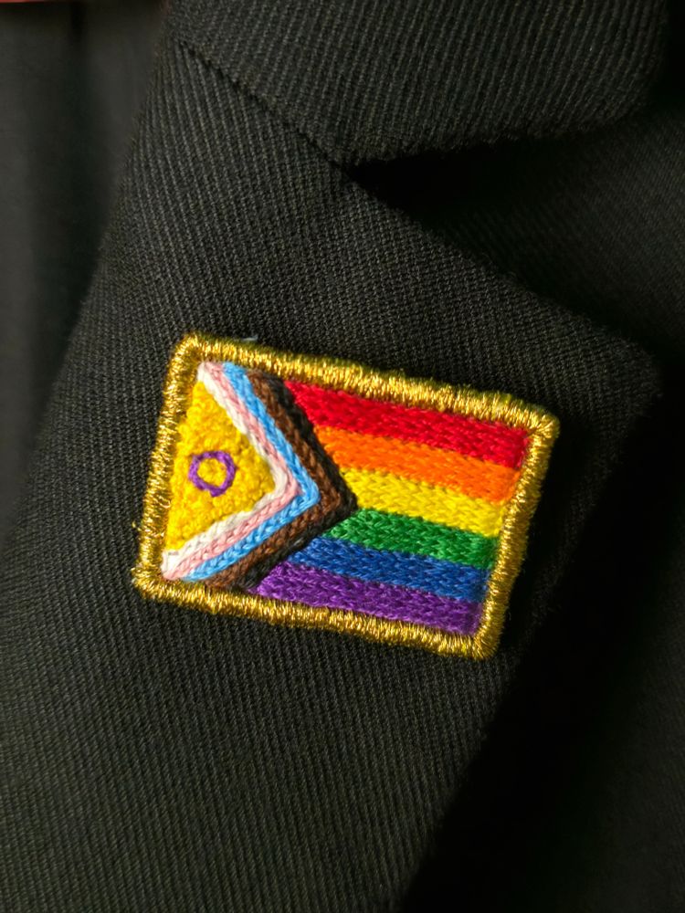 Pride flag lapel pin on a black blazer.
