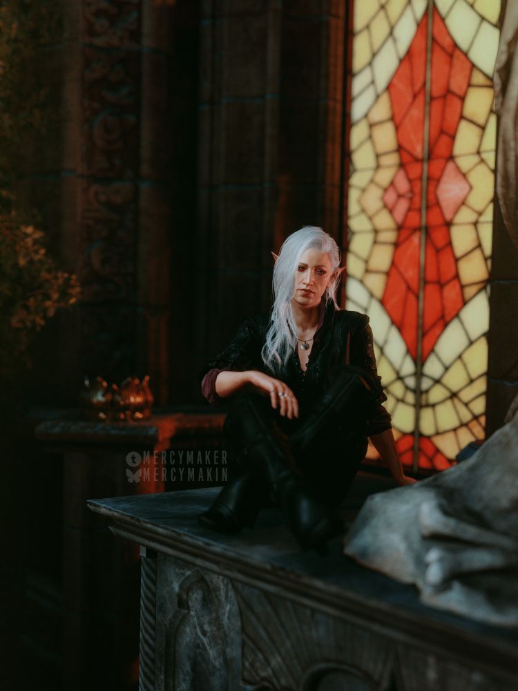 A virtual photography shot of Femstarion sitting on stone table in front of a red-yellow stained glass window. She sits cross-legged with a somber expression on her face.