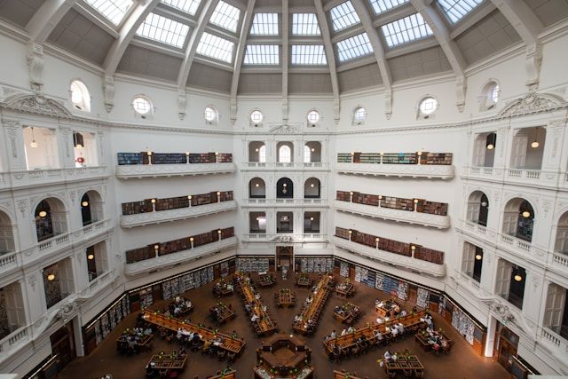 A photo of a hexagonal building with a glass arched ceiling. It's a library with wooden desks in a start shape. It looks peaceful and beautiful. 