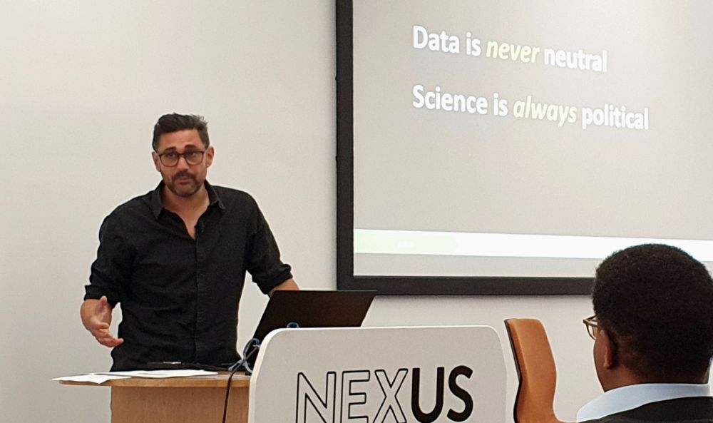 Adam Rutherford at a podium in front of a screen saying: Data is never neutral. Science is always political.