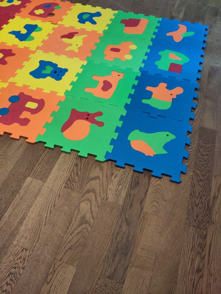 Ein Holzfußboden auf dem eine bunte Puzzlematte für Kinder liegt mit Tiermotiven