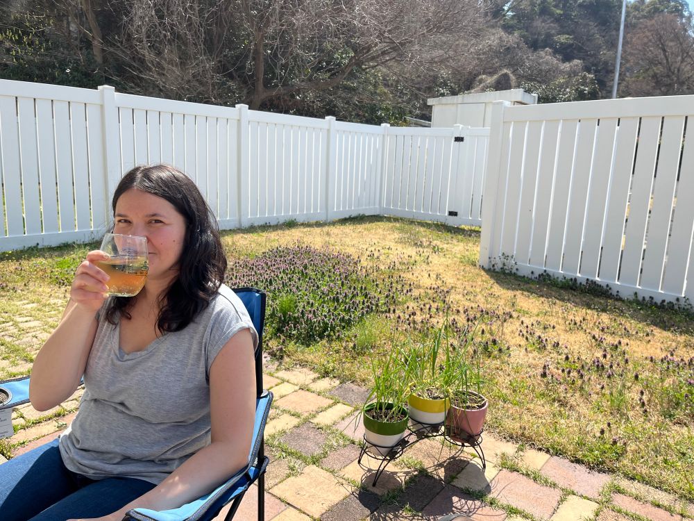 Mollie enjoys a wine spritzer. In the background, an unmoved yard full of flowers.