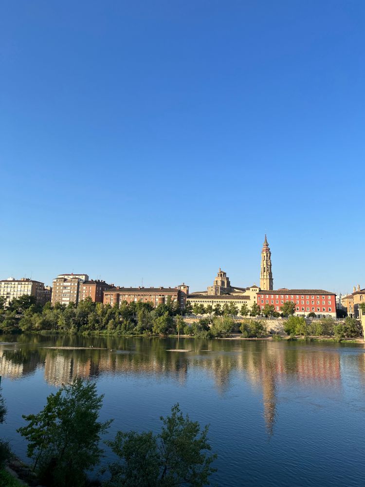 Vue de Zaragoza, depuis une des rives de l’Èbre, le ciel est bleu au dessus de nous
Devant nous on voit l’eau de l’Ebre, de l’autre côté il y a des bâtiments anciens