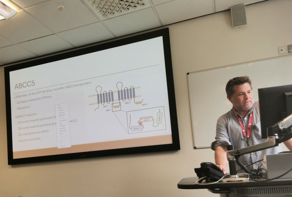 Dr Gareth Banks stands at a lectern explaining a slide describing ABCC5