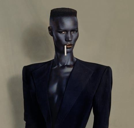 Grace Jones in a black suit and blue makeup to look as black and sharp and gleaming as obsidian, flat top, a white cigarette dangling from red/purple lips. One of the most perfect photos ever taken. Grace Jones by Jean-Paul Goude, for the album Nightclubbing, 1981