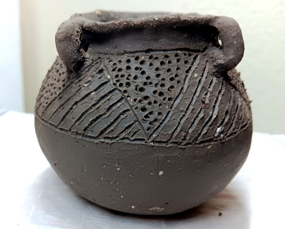 Dark gray-brown globular pot with 4 loop handles, a short neck & out-flared rim. The upper body is decorated with alternating triangles filled with diagonal parallel incised lines & stipple punctations.