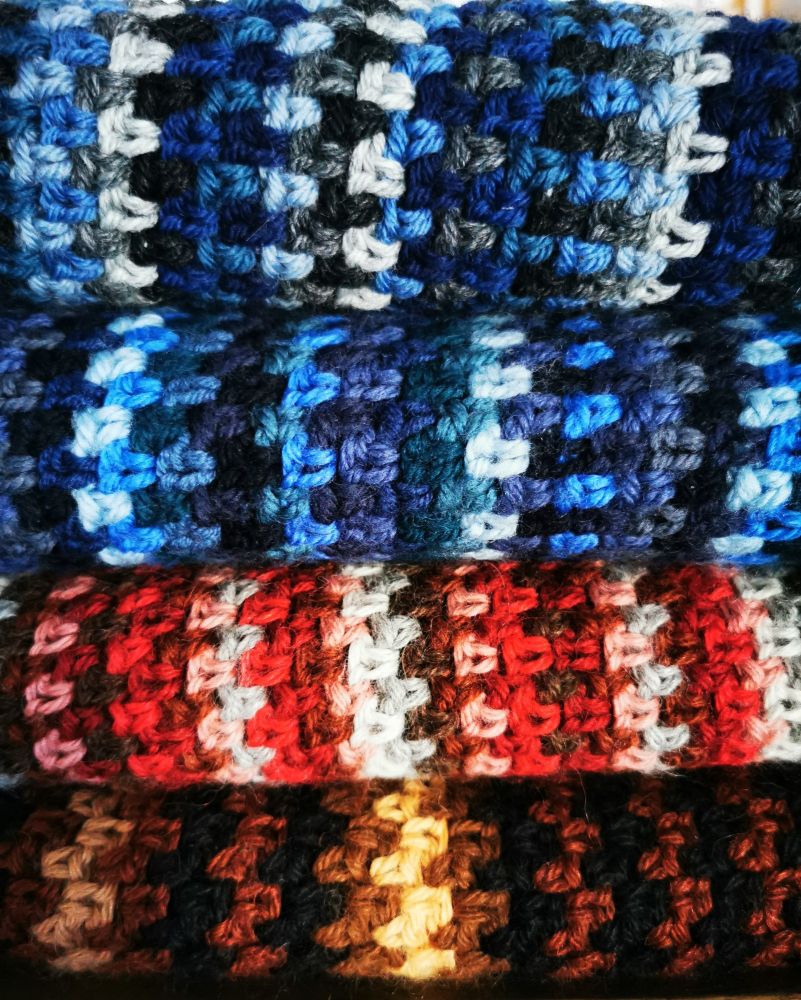 Pile of four colourful crocheted scarves in brown, red and blue tones.
