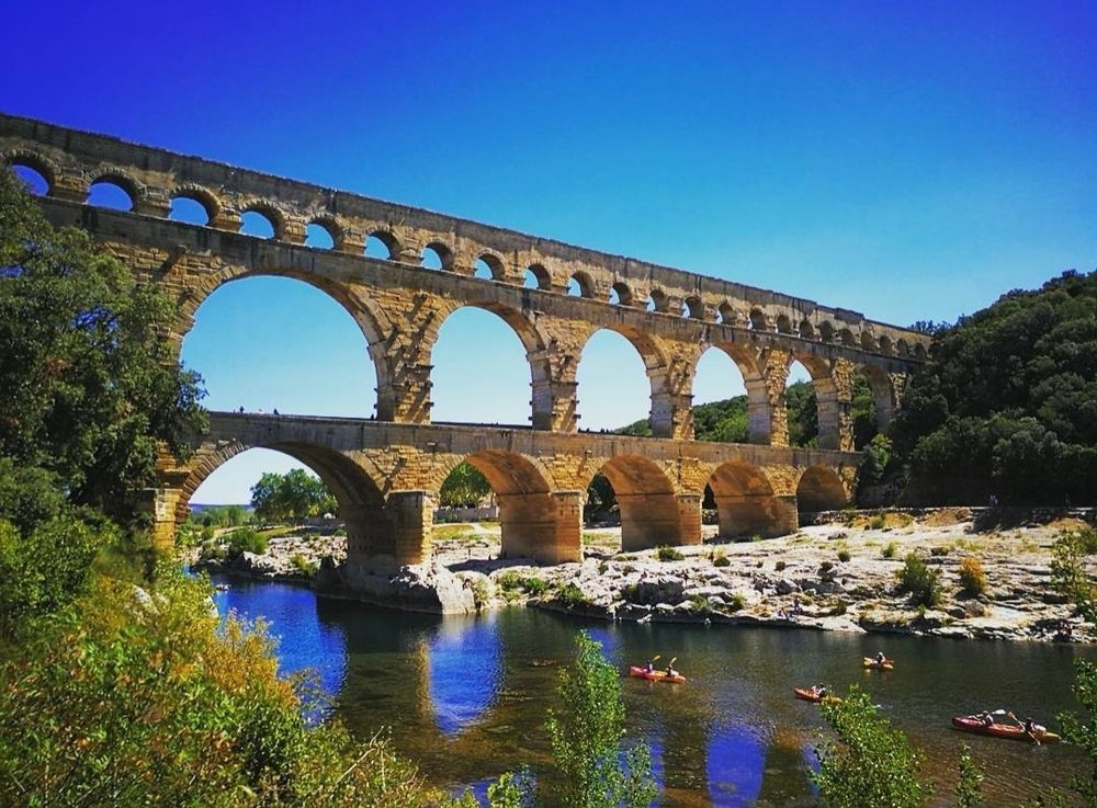 Roman aquaduct set against a blue sky with several small boats or kayaks in the water beneath.