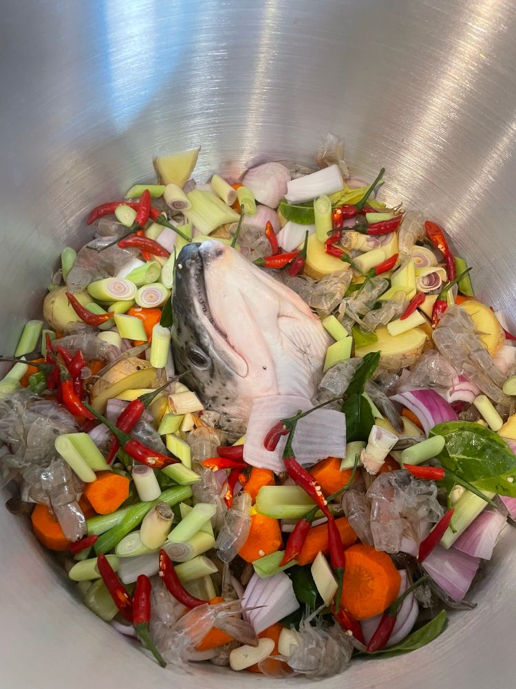 A salmon head surrounded by shrimp exoskeleton and vegetables. 