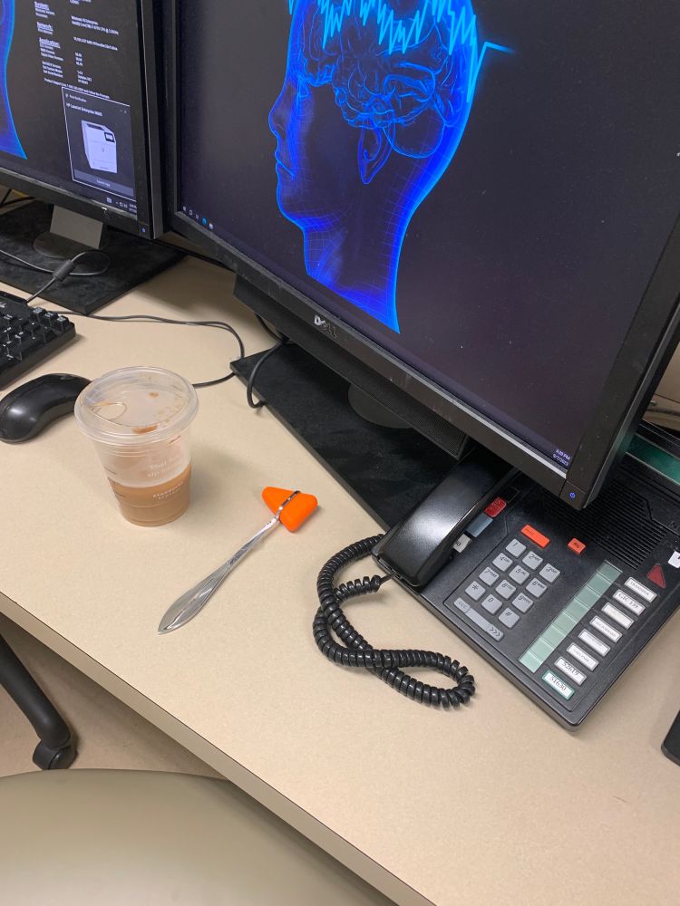 A desk with a computer on it as well as a triangle reflex hammer.