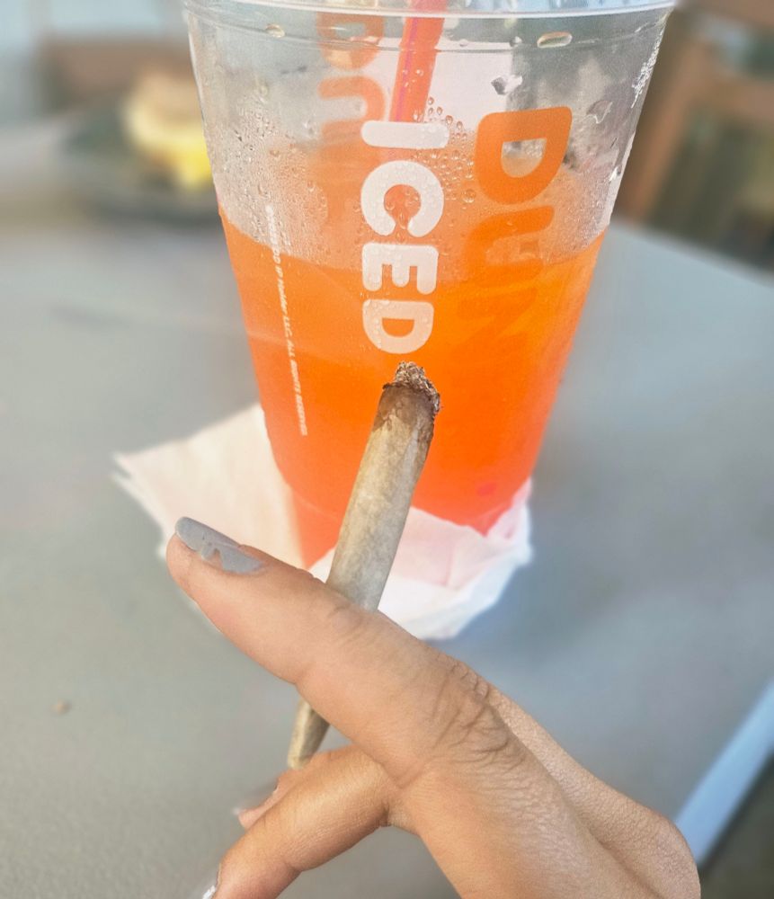 user's hand holding a joint in front of an iced drink from dunkin donuts