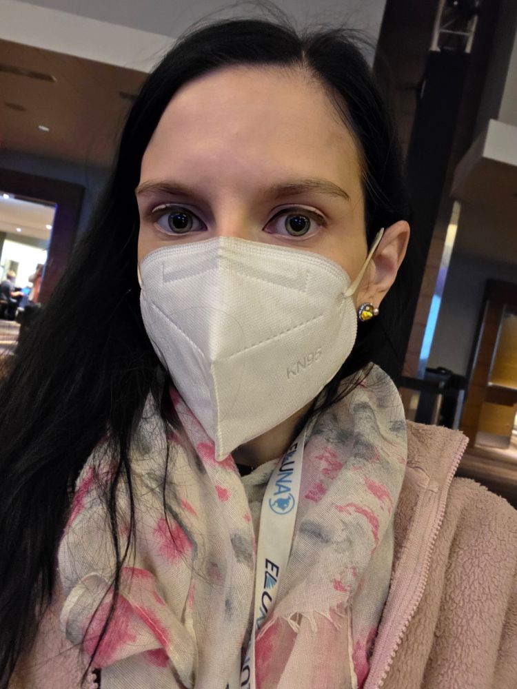 White woman with black hair wearing a mask and pink fleece jacket