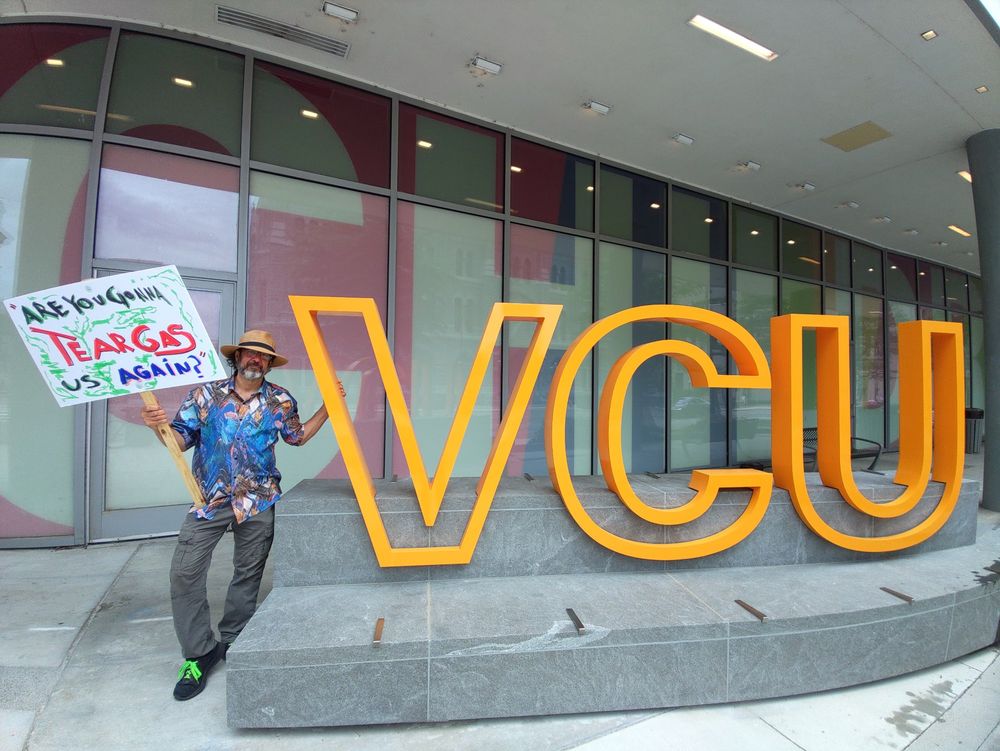 Photo of Arthur Brill holding sign reading "are you gonna tear gas us again?" In quotes next to VCU sign in Richmond, Virginia