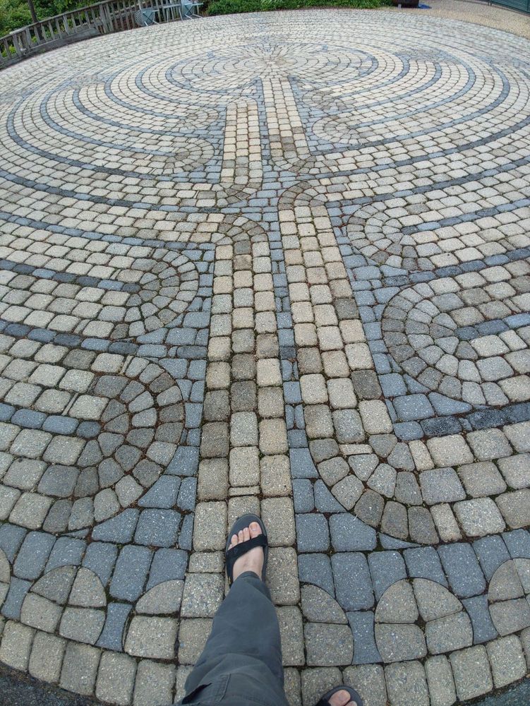 Photo of a labyrinth  created with mosaic brickwork, with a foot one step forward in to begin the journey