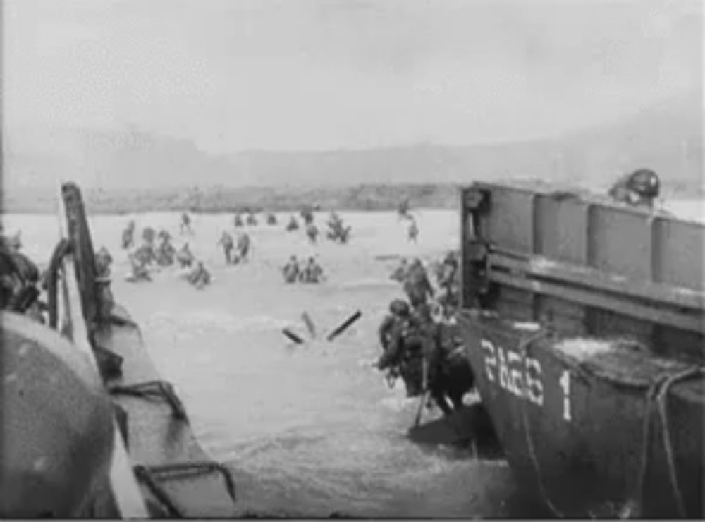 a black and white photo of a group of soldiers getting off a boat in the ocean .