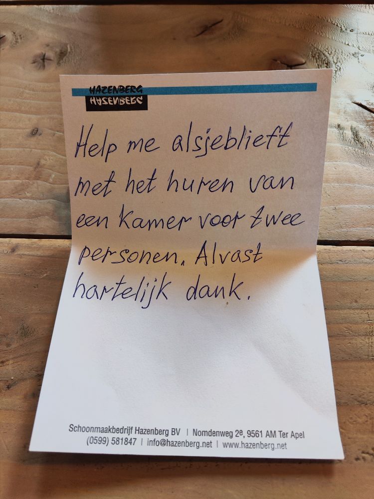 Een notitiebriefje met het logo van schoonmaakbedrijf Hazenberg waarop in een keurig handschrift geschreven is: Help me alsjeblieft met het huren van een kamer voor twee personen. Alvast hartelijk dank.