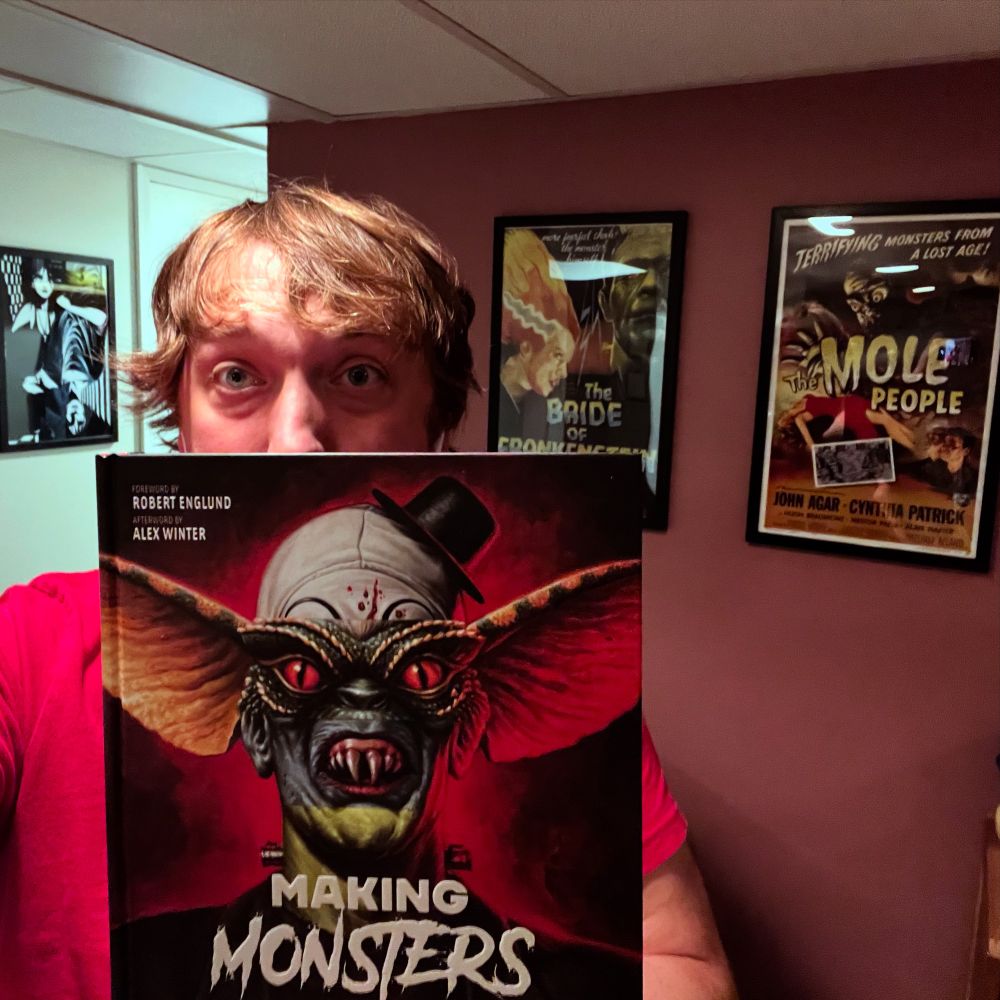 Image of a man holding the book ‘Making Monsters.’ Backdrop includes posters of ‘The Bride of Frankenstein,’ and ‘The Mole People.’