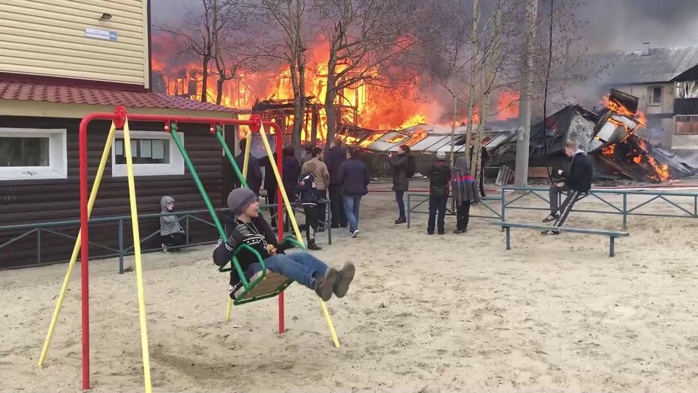 Kid on swing in front of burning house.