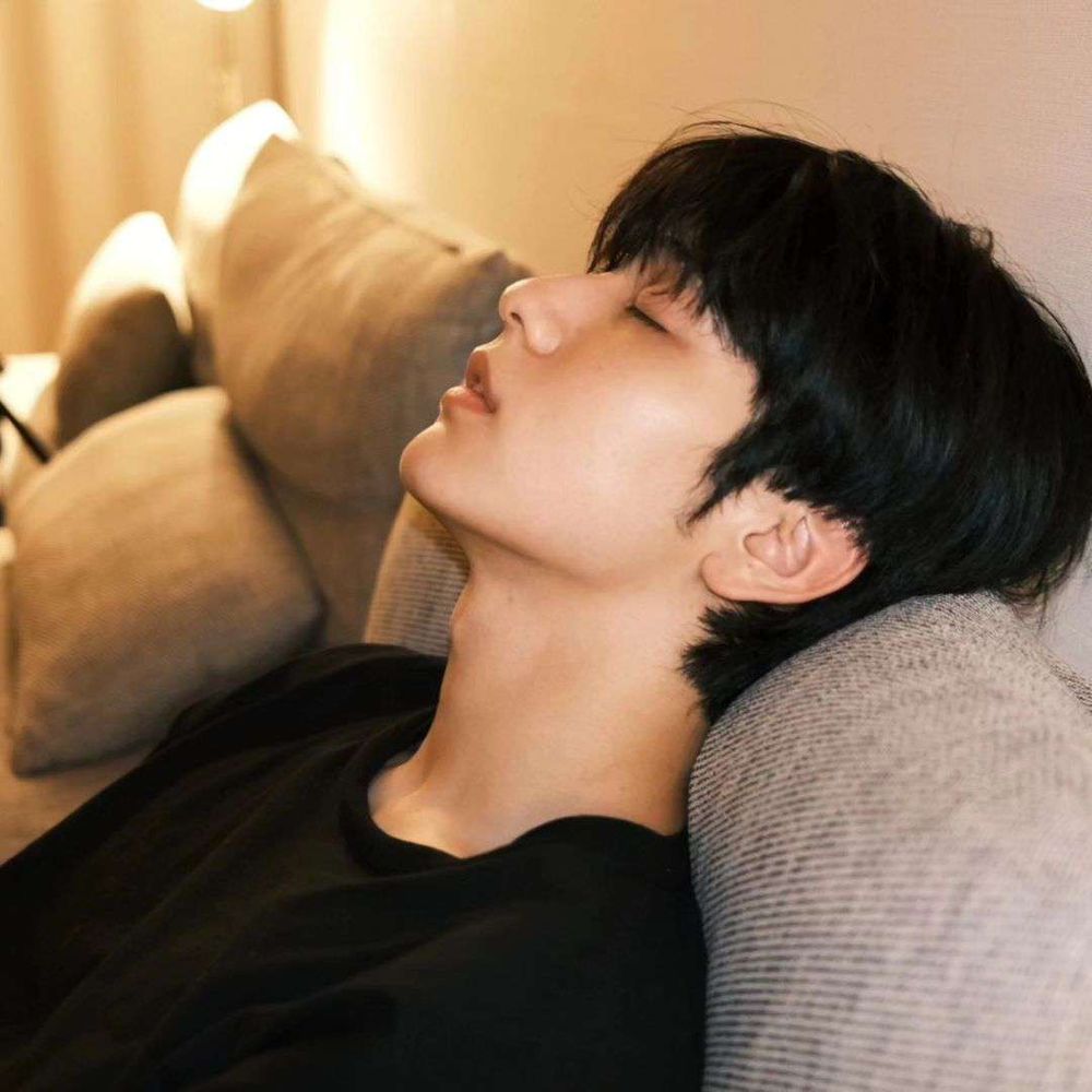 picture of choi soobin from tomorrow x together. he has black hair, is wearing a black t-shirt and is leaning back on a light grey couch. a warm light is shining in the background. his head is resting back against the cushions, his eyes closed and his mouth slightly open. it's about as devastating as that sounds tbh.