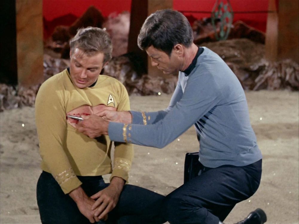 kirk and mccoy in the star trek episode "amok time." mccoy is giving kirk an injection and touching his chest