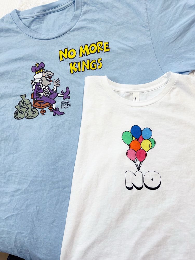 Two t-shirts, a blue one reading “ano more Kings” with a cartoon drawing of King George III sitting on a stool with bags of money from Schoolhouse Rock. The second is a white shirt with multicolored balloons on top the word “No”.