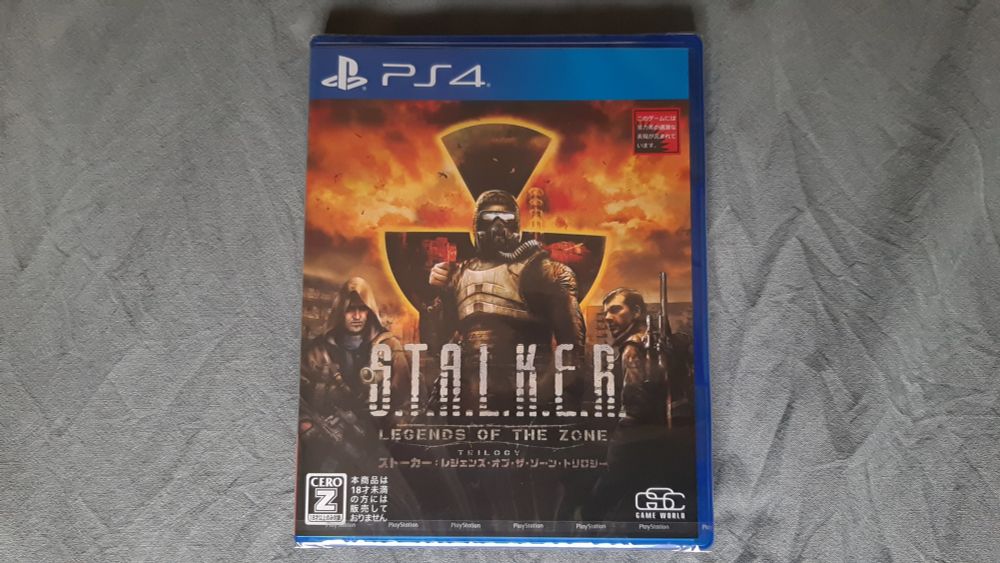 Japanese PS4 game box for S.T.A.L.K.E.R. - Legends of the zone with a man in armor and with visor on, two other characters to the side and a large fire with a radiation shape in it in the background.