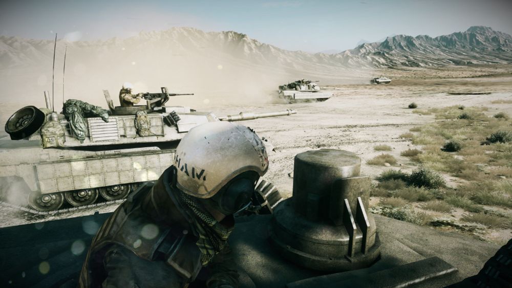 Point of view from a tank with other tanks in the background driving over a large open field with mountain ranges in the background.
