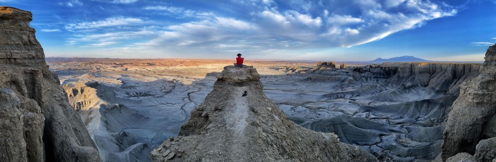 A woman sits alone on a rocky outcropping of stone overlooking a barren landscape far below.