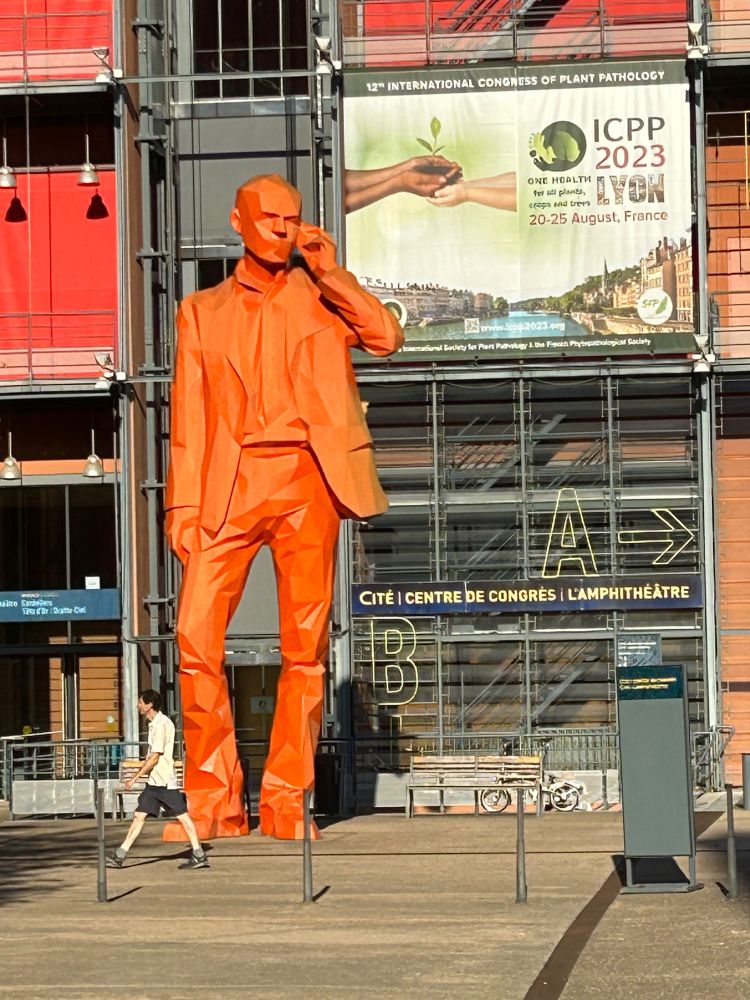 Giant orange man (statue) standing in front of the ICPP banner outside of the Lyon Convention Center