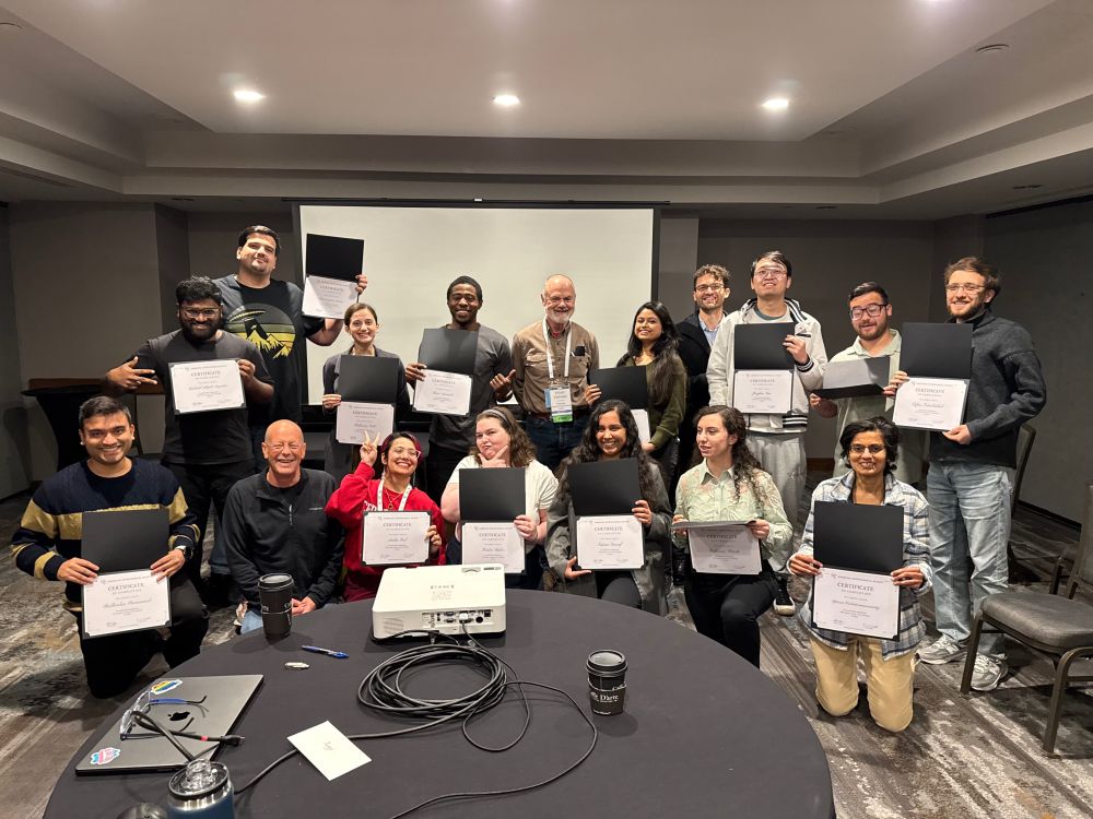 Group of young astronomers smiling and  holding certificates and two old bald guys.