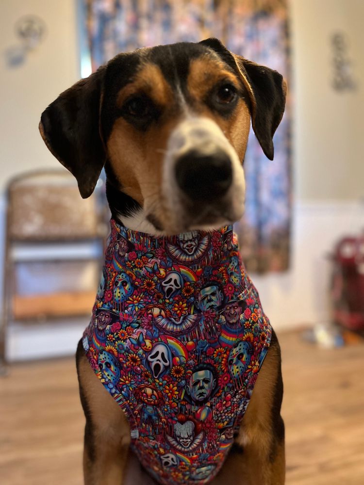 Tricolor hound in a neon muscle shirt with artwork of Michael Myers, Freddy Krueger, Jason, Chucky, Ghostface, and Pennywise, with rainbows, flowers, and butterflies 