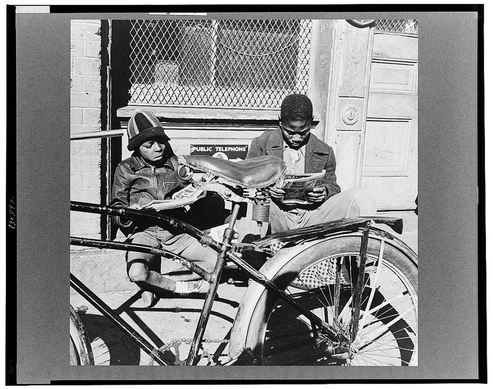 Two black youths read copies of Police Comics (May 1942), while sitting on a building stoop in Southwest Washington, DC. Photograph by Gordon Parks, November 1942, for the Farm Security Administration.