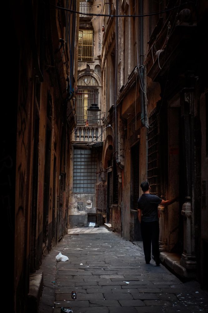 Dark alley in Genova Italy with a man trying opening his door in the dark. At the end af the alley lights behind the windows.