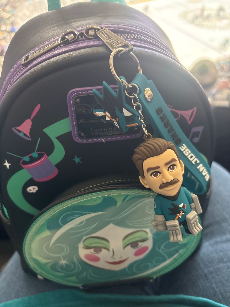 The same bag tag from the first post, with San Jose Sharks teal strap, San Jose Sharks logo, and mustached goalie figure, but now it’s hooked onto the zipper of a loungefly mini backpack that’s Madame Leota (from Disneyland’s Haunted Mansion) themed where her face in the crystal ball is the front of the small front pocket