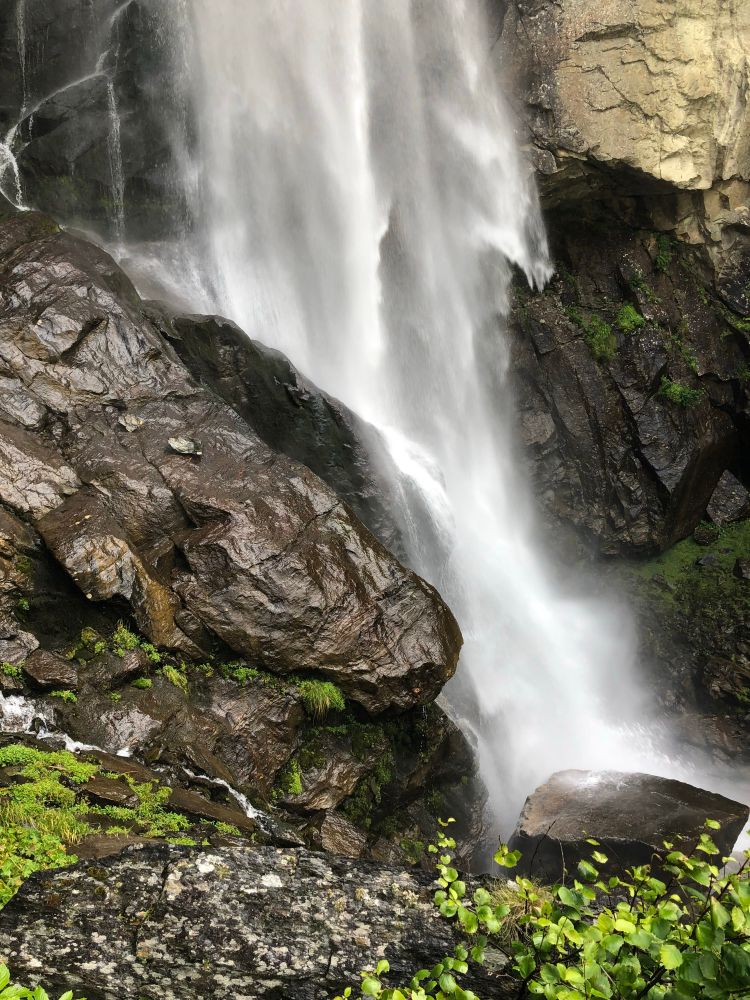 The photo shows the bottom section of a large waterfall as it crashes onto the wet, dark rocks at the base of the falls.